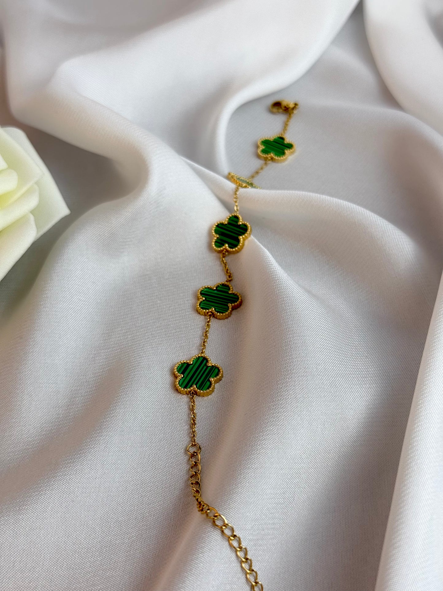 Gold bracelet with green clover charms on a white fabric background