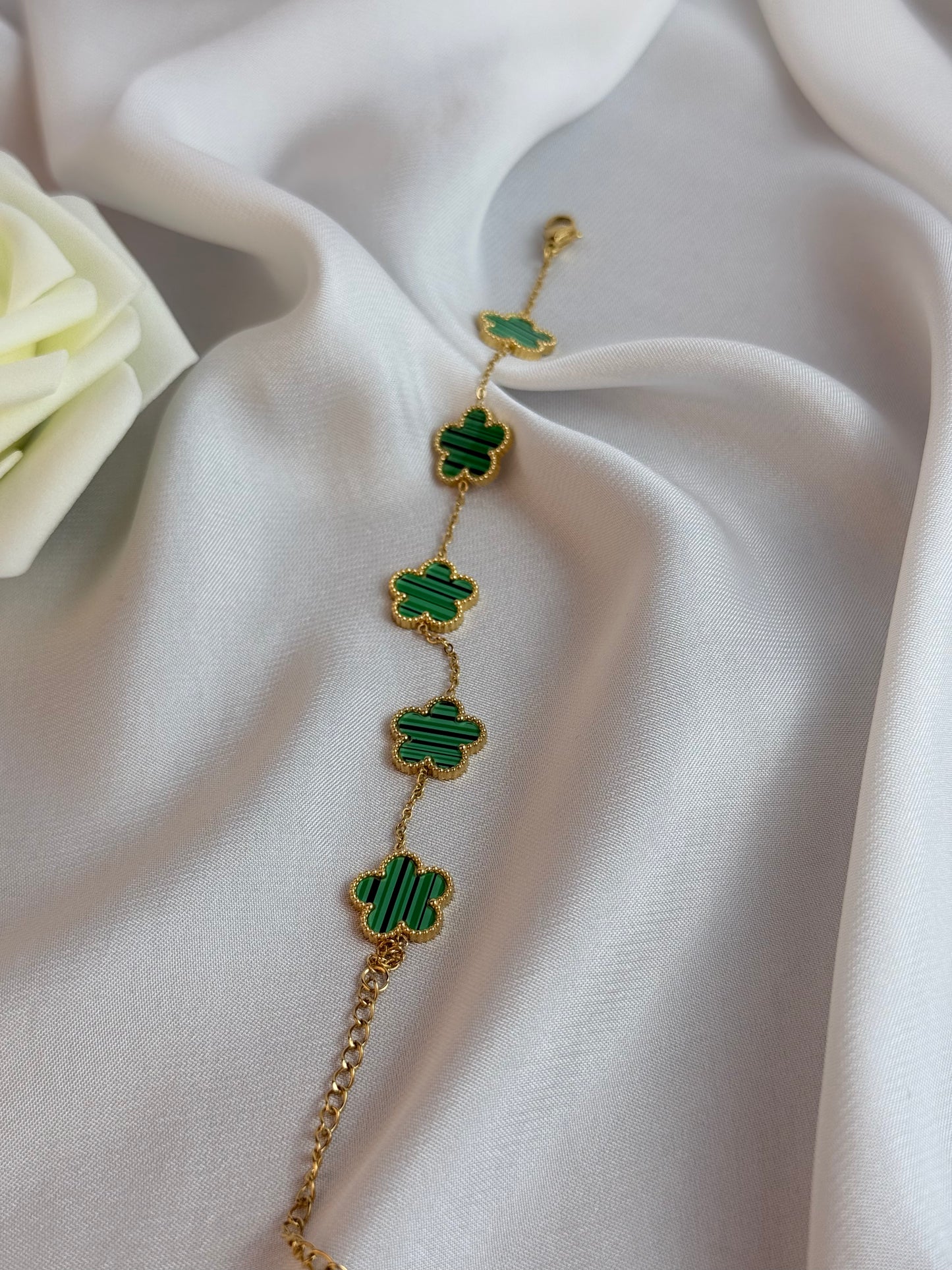 Gold bracelet with green clover-shaped charms on a white fabric background