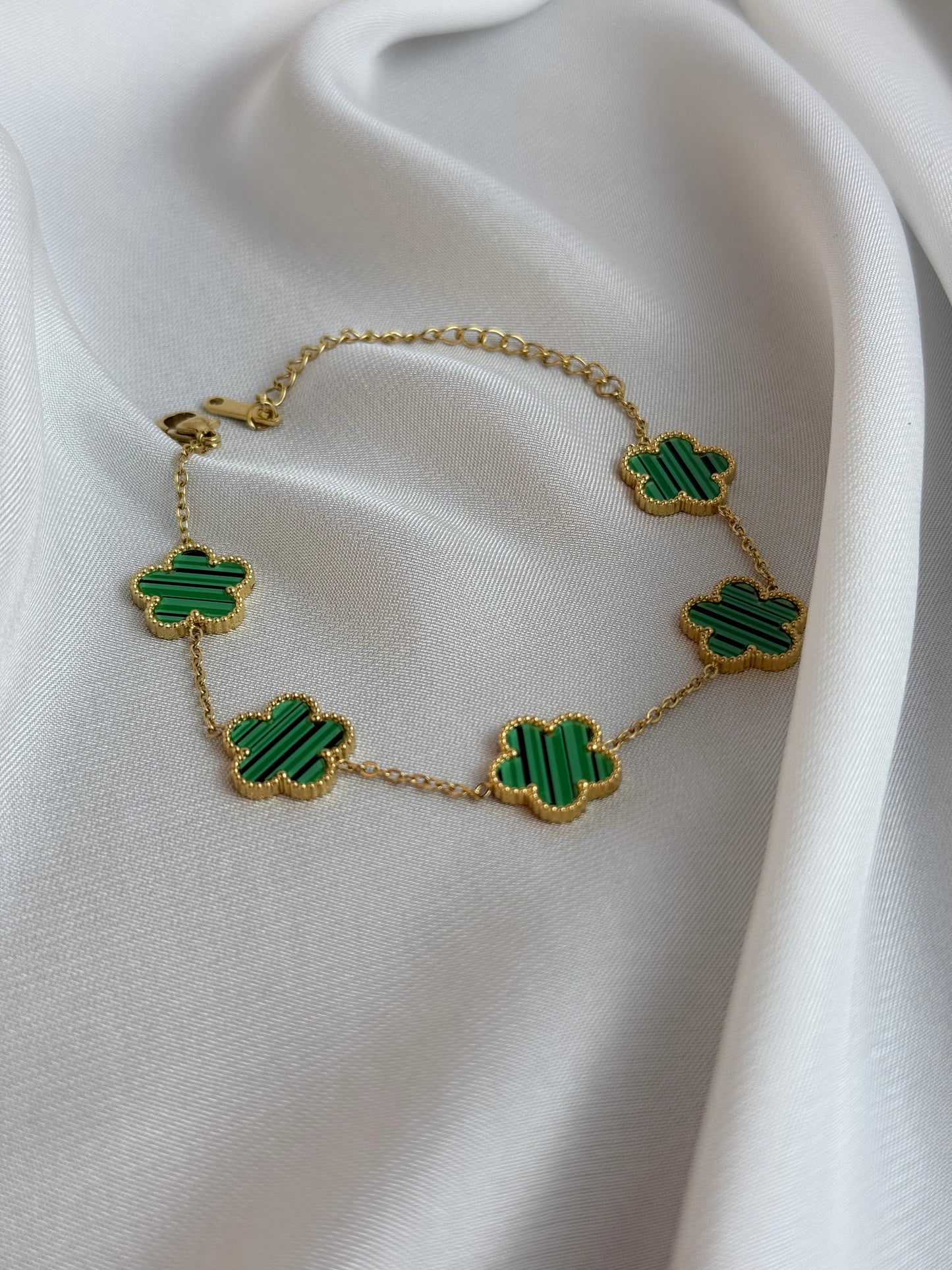 Gold necklace with green clover-shaped pendants on a white fabric background