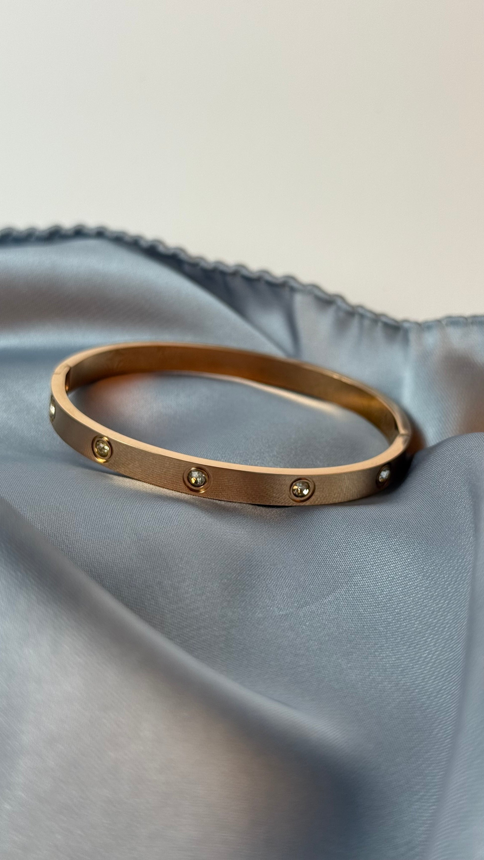 Gold bracelet with small stones on a light blue fabric background