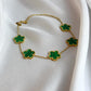 Gold necklace with green clover-shaped pendants on a white fabric background