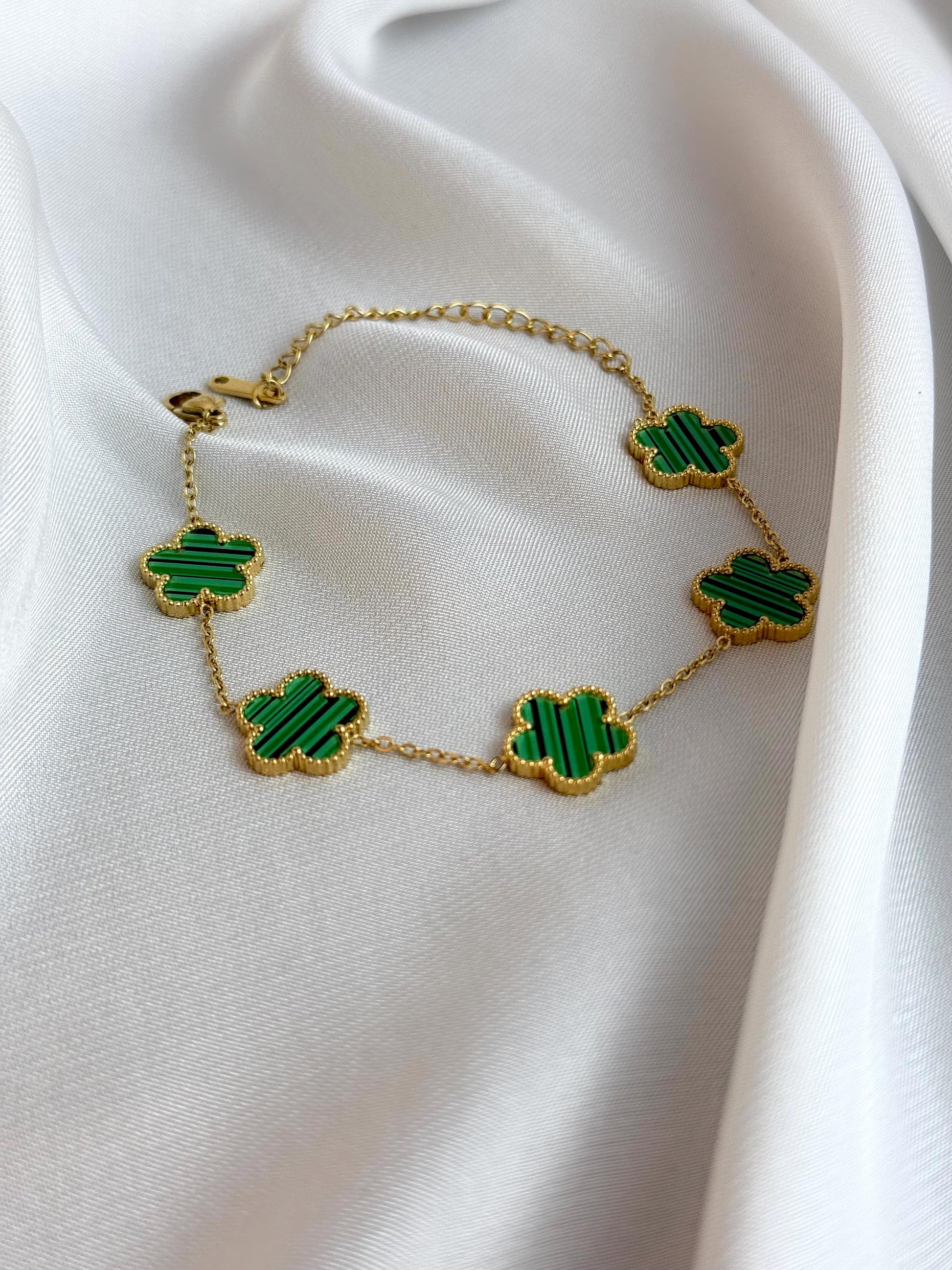 Gold necklace with green clover-shaped pendants on a white fabric background