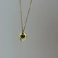 Gold necklace with a round pendant featuring a blue gemstone on a gray background