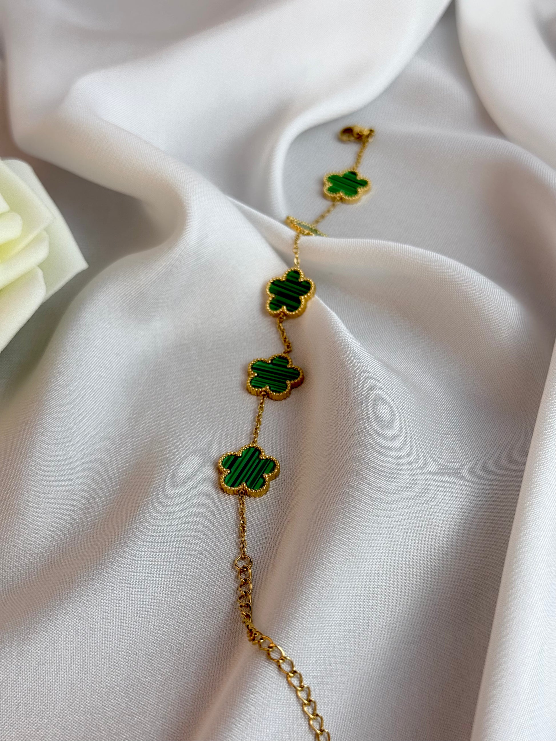 Gold bracelet with green clover charms on a white fabric background