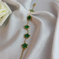 Gold bracelet with green clover-shaped charms on a white fabric background