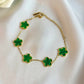 Gold bracelet with green clover-shaped charms on a white fabric background