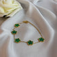 Gold bracelet with green clover-shaped charms on a white fabric background