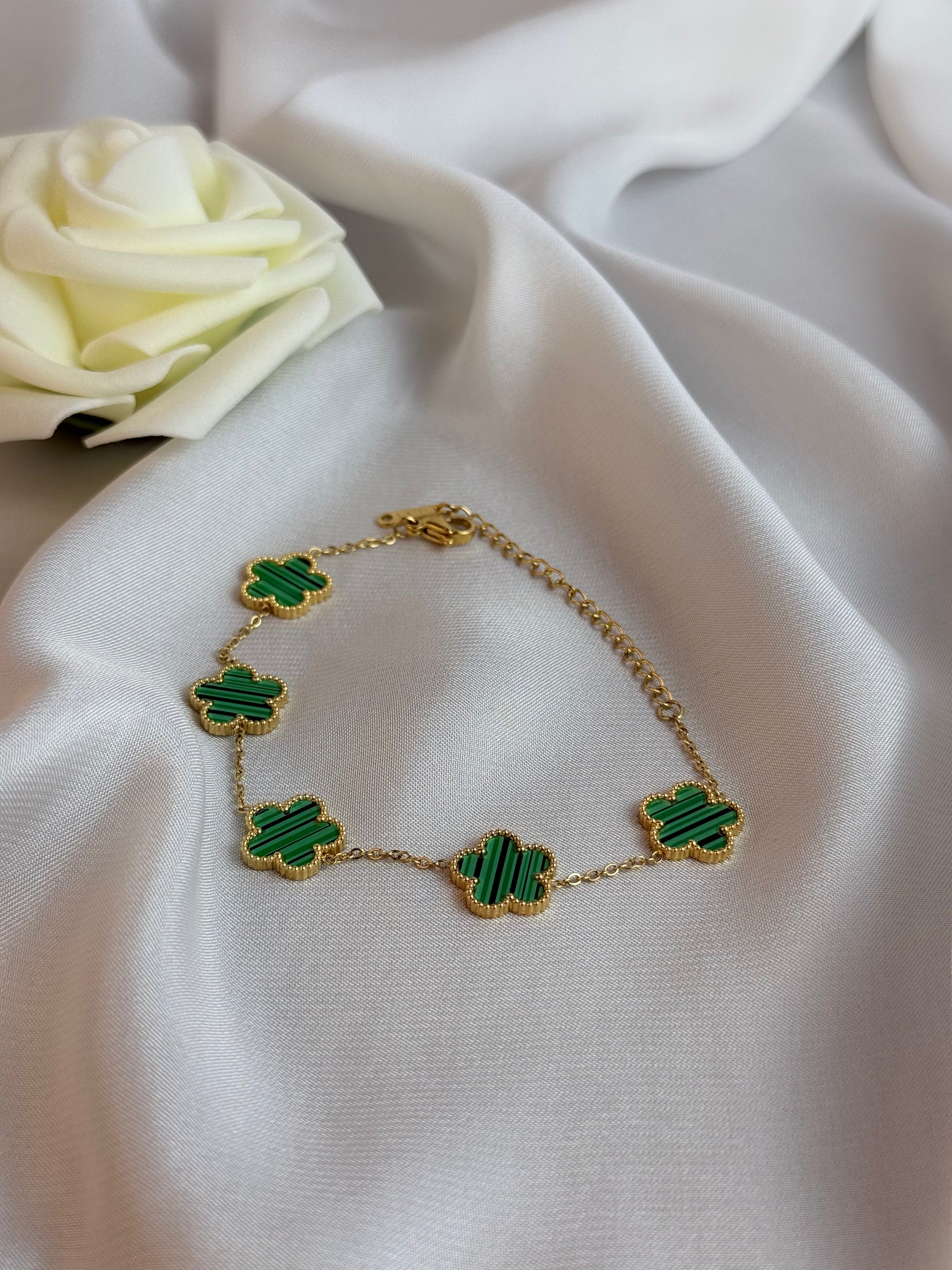Gold bracelet with green clover-shaped charms on a white fabric background