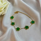 Gold bracelet with green clover-shaped charms on a white fabric background