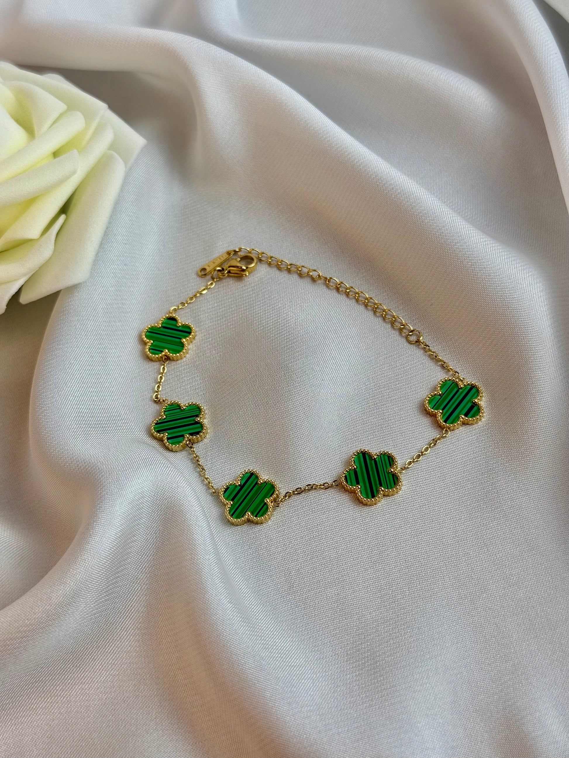 Gold bracelet with green clover-shaped charms on a white fabric background
