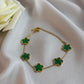 Gold bracelet with green clover-shaped charms on a white fabric background