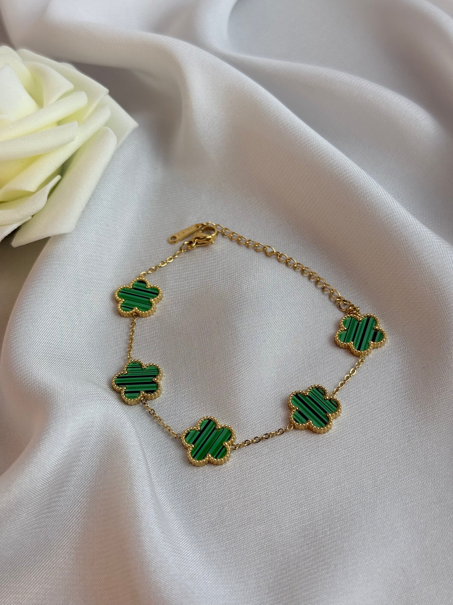 Gold bracelet with green clover-shaped charms on a white fabric background