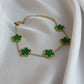 Gold necklace with green clover-shaped pendants on a white fabric background