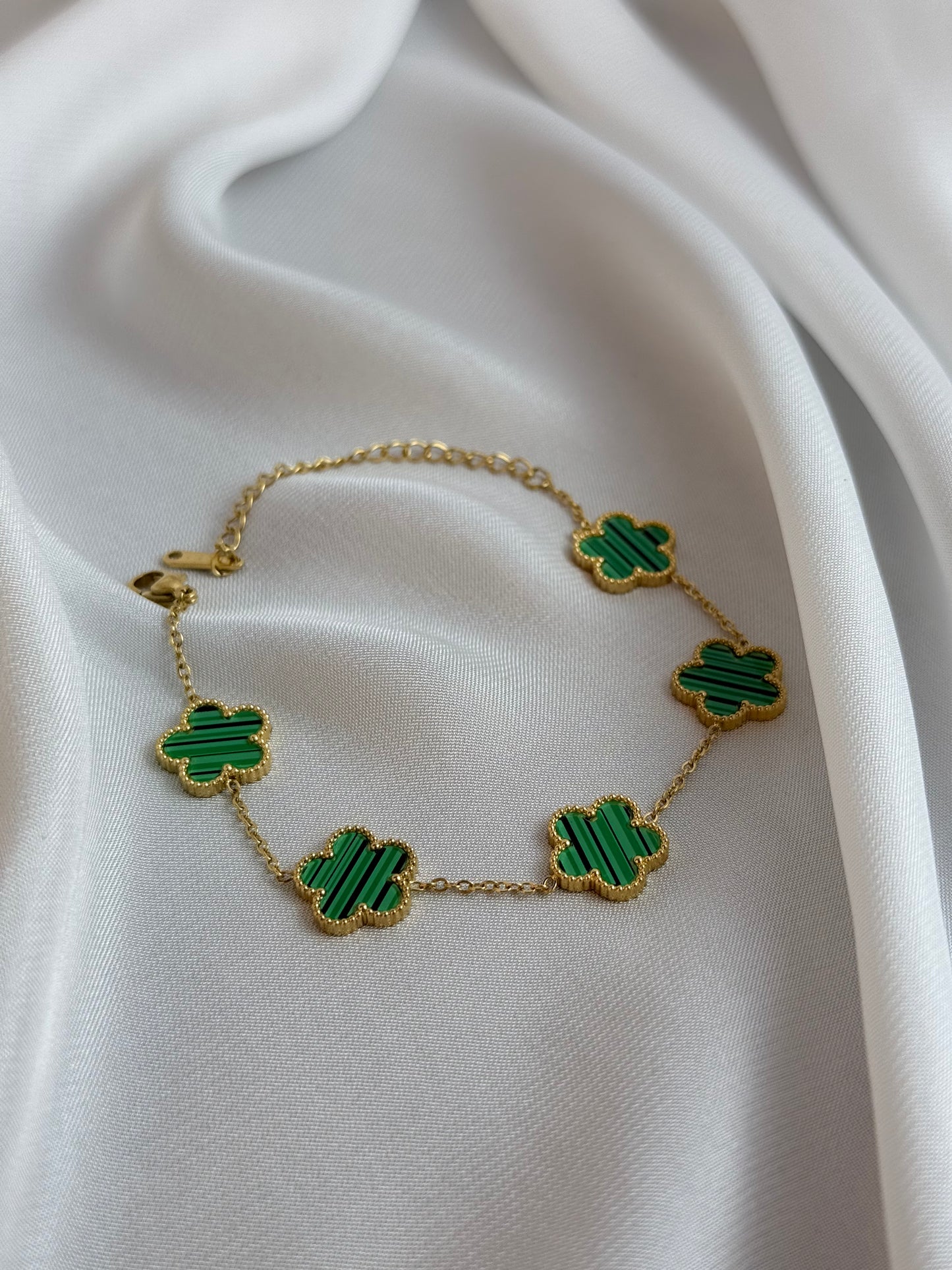 Gold necklace with green clover-shaped pendants on a white fabric background