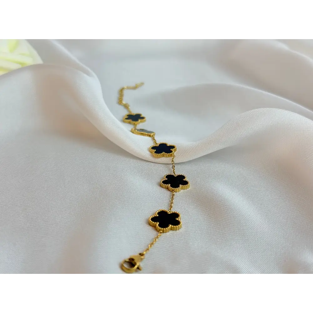 Gold necklace with black clover-shaped pendants on a white fabric background