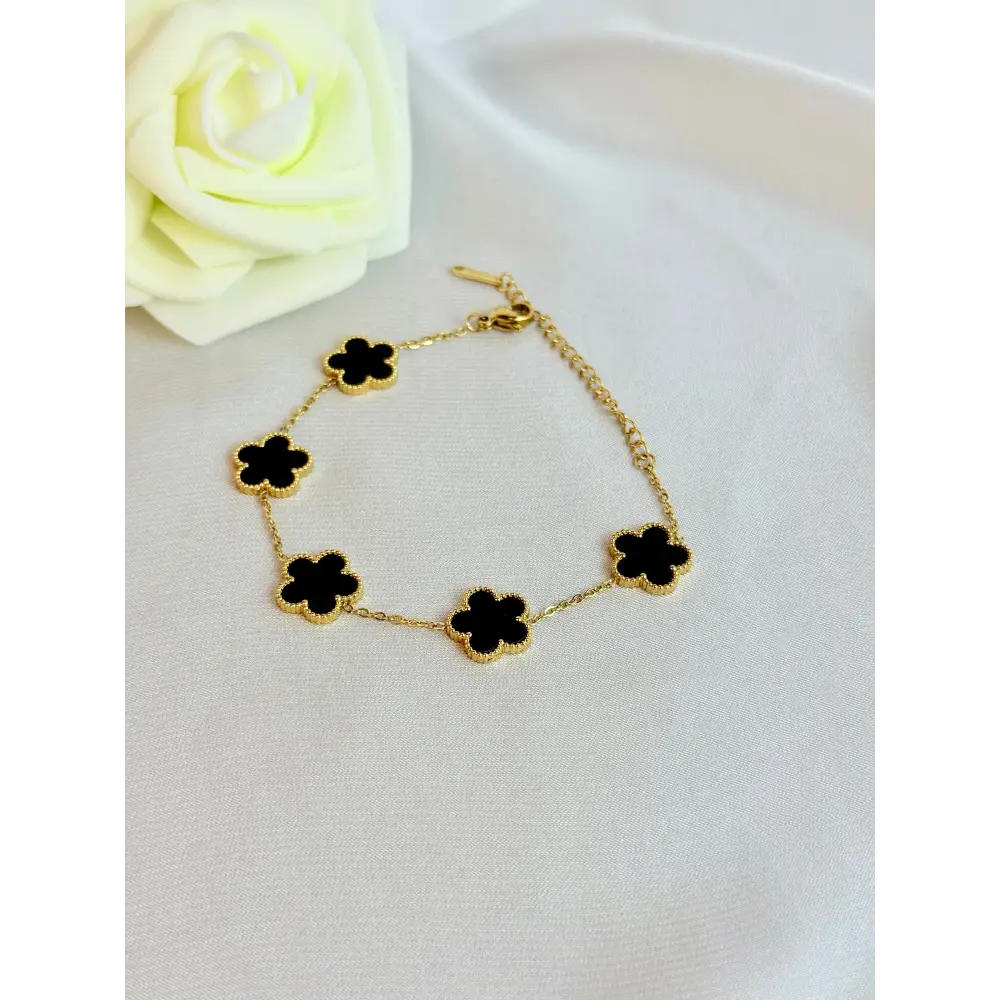 Gold bracelet with black clover-shaped charms on a white surface with a white rose.