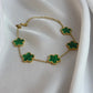 Gold necklace with green clover-shaped pendants on a white fabric background
