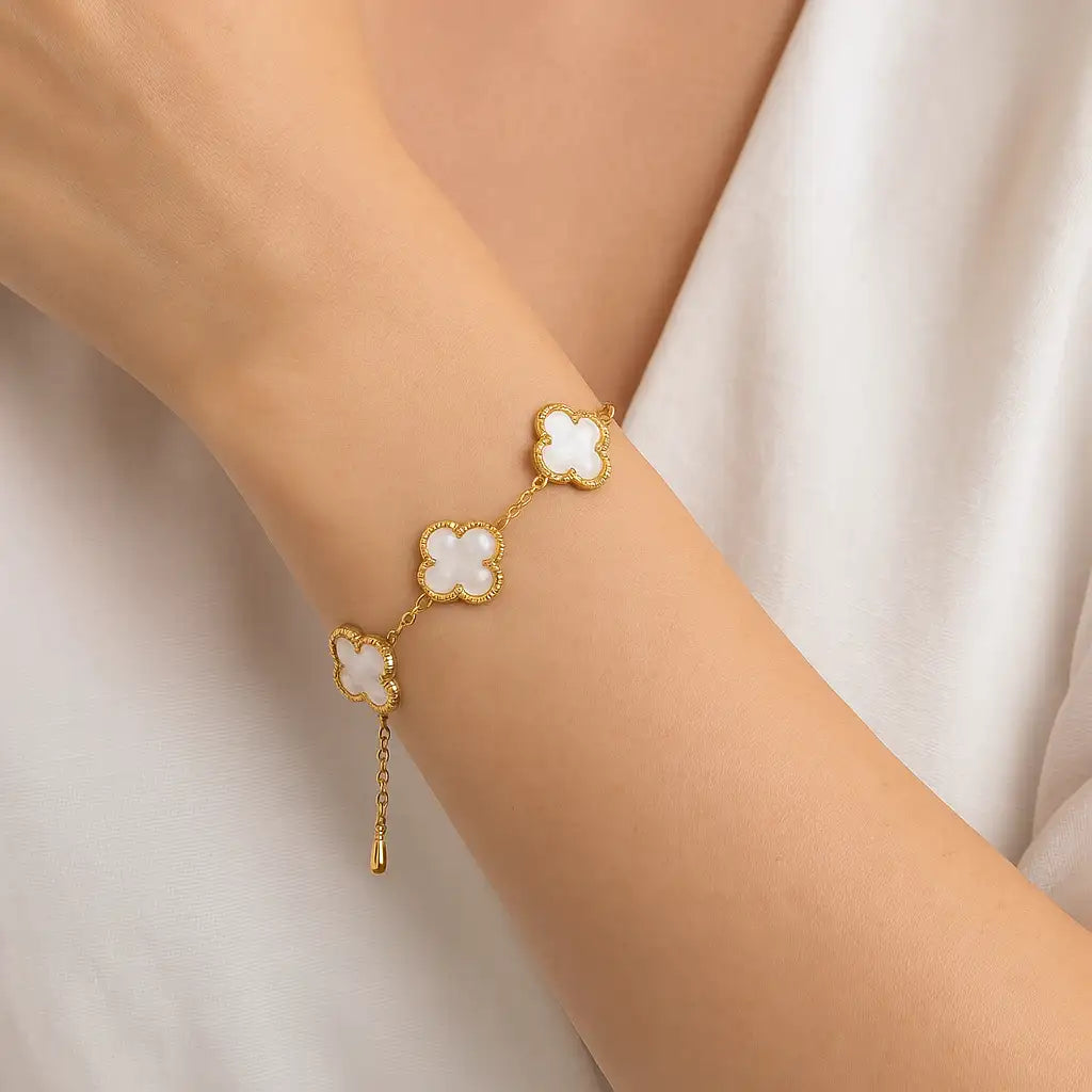 Gold-toned bracelet featuring three clover-shaped links with white mother-of-pearl inlays and a delicate chain extending to a small dangling teardrop charm.
