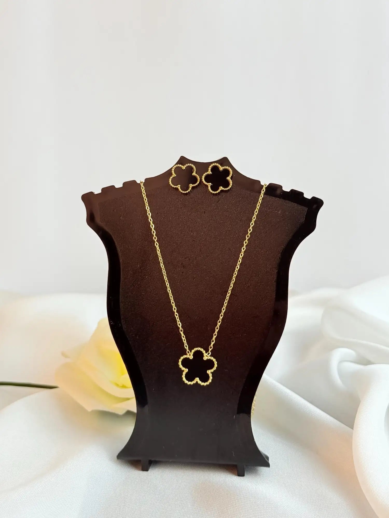 Gold-toned four-leaf clover necklace and matching earrings displayed on a dark brown mannequin bust.