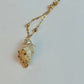 Gold necklace with a shell pendant on a light gray background