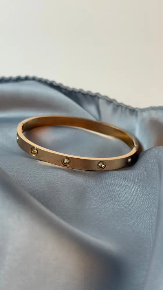 Gold bracelet with small stones on a light blue fabric background